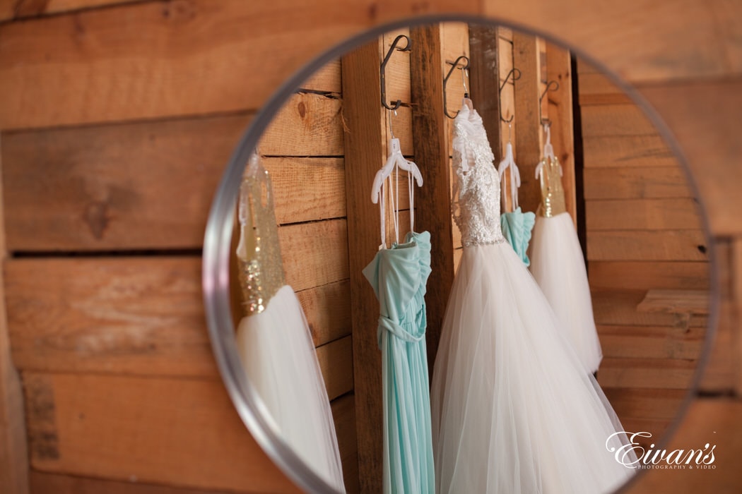 In this mirrored image are the bride's, bridesmaids', and flower girls' dresses. All lovely placed among a rustic wooden wall.