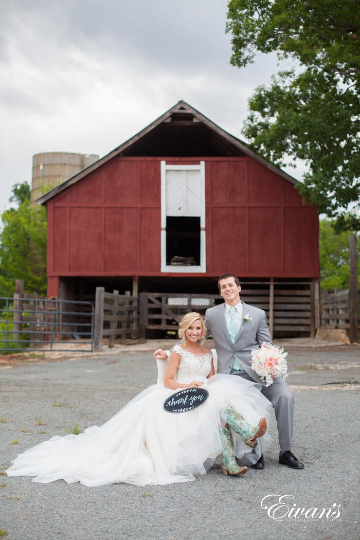The couple sits together in front of a beautiful and rustic barn celebrating their love together.