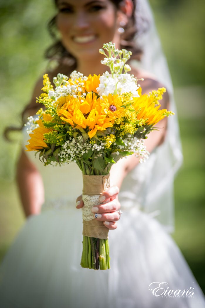 Holding her rustic bouquet made of classic white flowers and vibrant sunflowers.