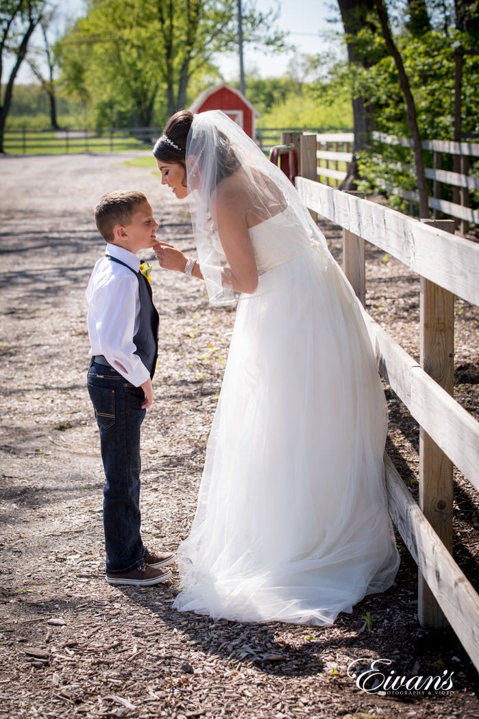 Going to kiss the head of the little ring bearer while standing and leaning on a wood fence enjoying the sun and beautiful weather.