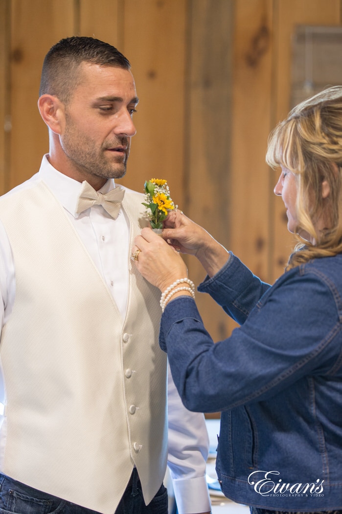 Placing a sunflower boutonniere on her son's and the groom's vest for his more then special day.