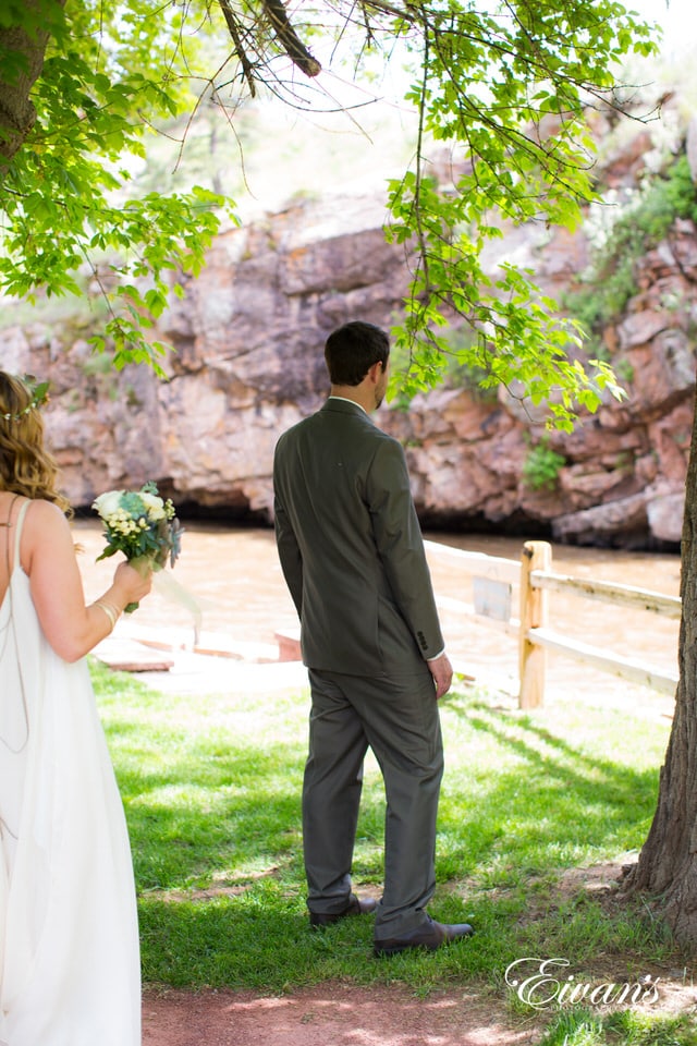 man in black suit and woman in white wedding dress kissing on green grass field during