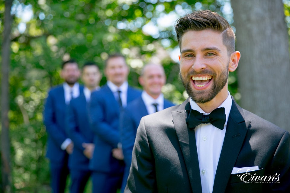 A groom smiles broadly in depth in field shot.