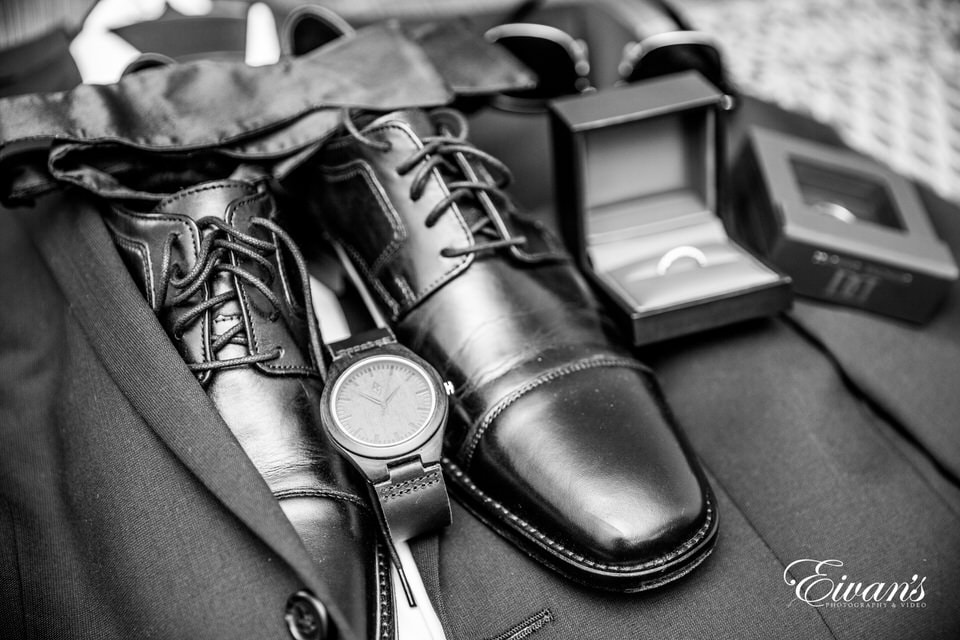 The photographer captures a detail shot of the groom's suit, shoes, watch, sunglasses, bowtie, and rings.