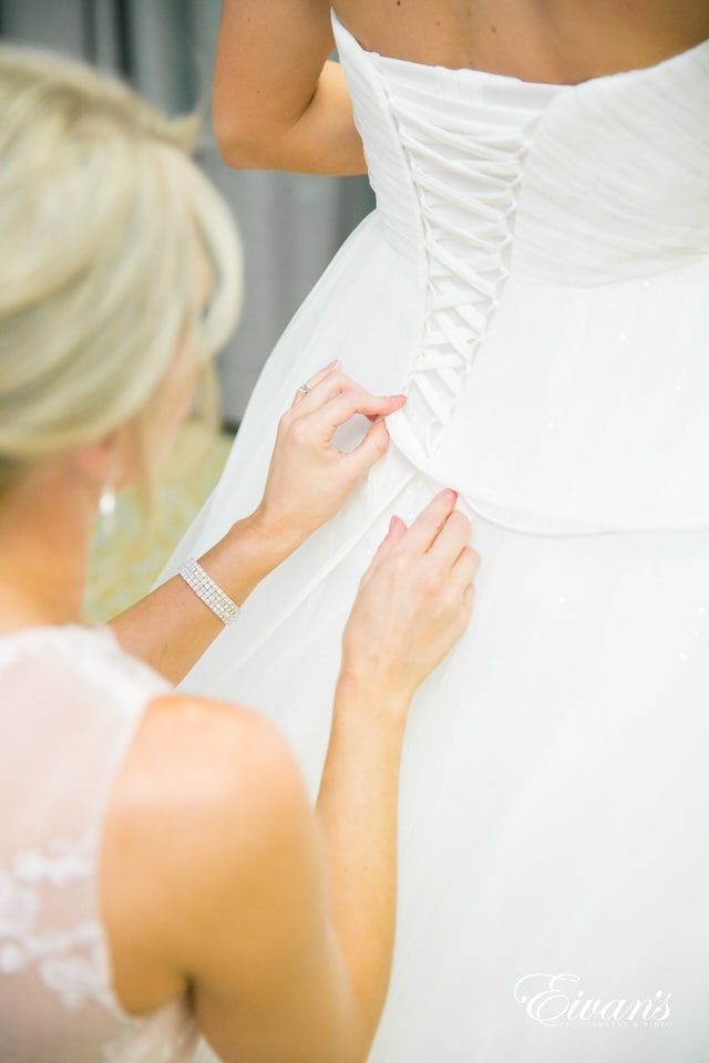 The mother of a bride carefully laces up her daughter's wedding dress.