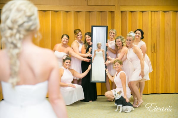 160625-grand-rapids-wedding-photos-26 The photographer captures a reflective photo of a bride smiling and looking into a rectangular mirror held by her excited bridal party. Her small, tuxedo-clad dog sits sweetly alongside the bridesmaids.