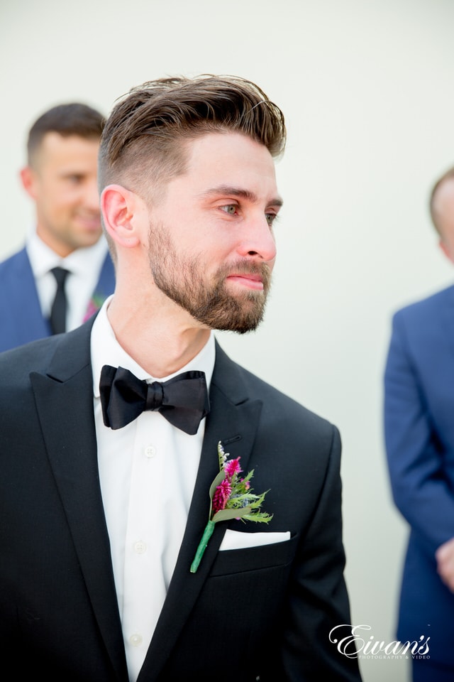 A groom is emotional after his wedding ceremony. He wears a black satin bowtie and a wildflower a boutonniere.