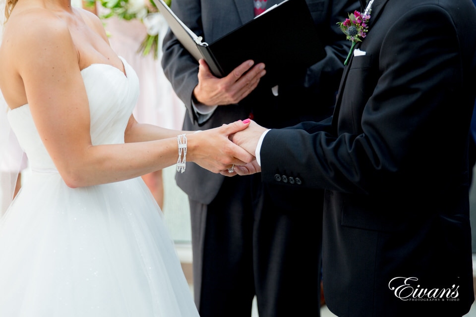 The photographer focuses on the hands of bride and groom during their ceremony as the officiant reads behind them.