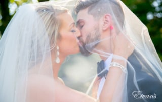 A bride and groom kiss under the cover of the bride's veil.