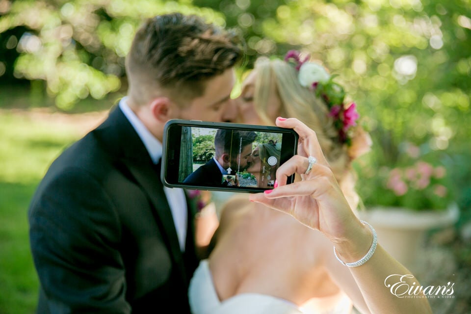 The photographer takes a portrait of a bride snapping a selfie of her and her new husband sharing a kiss.