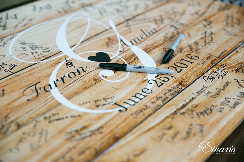 A detail wedding shot of the couple's names and wedding date on a large wooden poster decorated with the names and funny messages of their many guests.