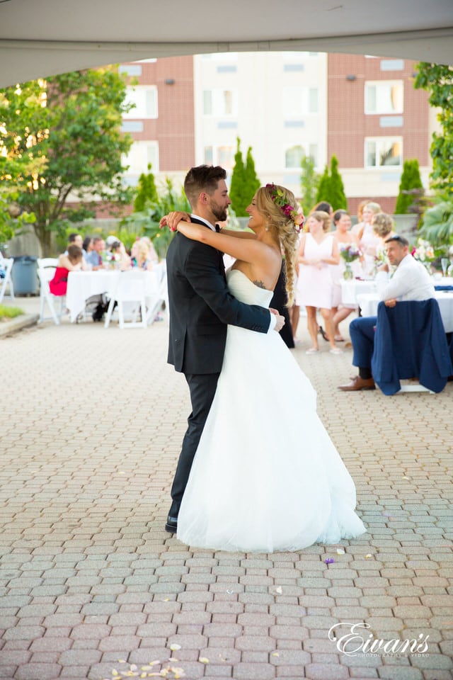 The bride and groom dance chest to chest while smiling at each other during their reception. The bridal party lingers in the background with the rest of the guests.