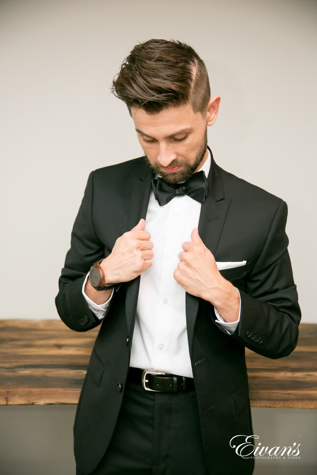 The groom cooly straightens his suit in a portrait style image.