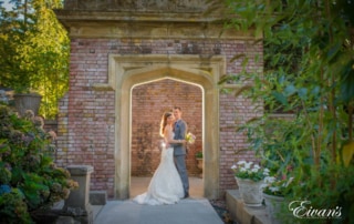 Newlyweds embrace each other beneath a well-lit entryway in the garden.