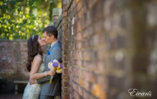 Bride and groom kiss against a brick wall.