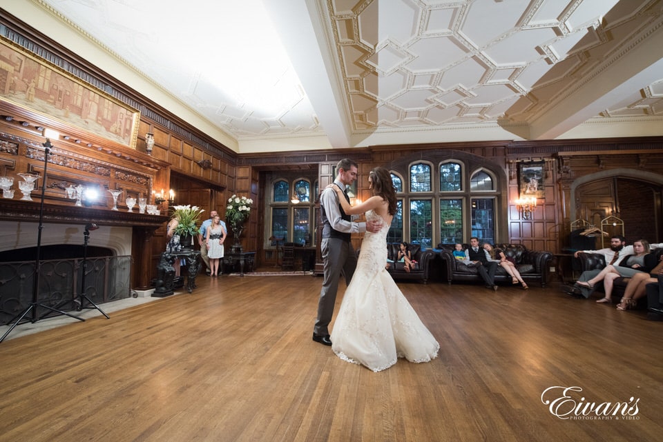 Bride and groom share a dance at their reception in an oldfashioned victorian styled home as onlookers watch leisurely.