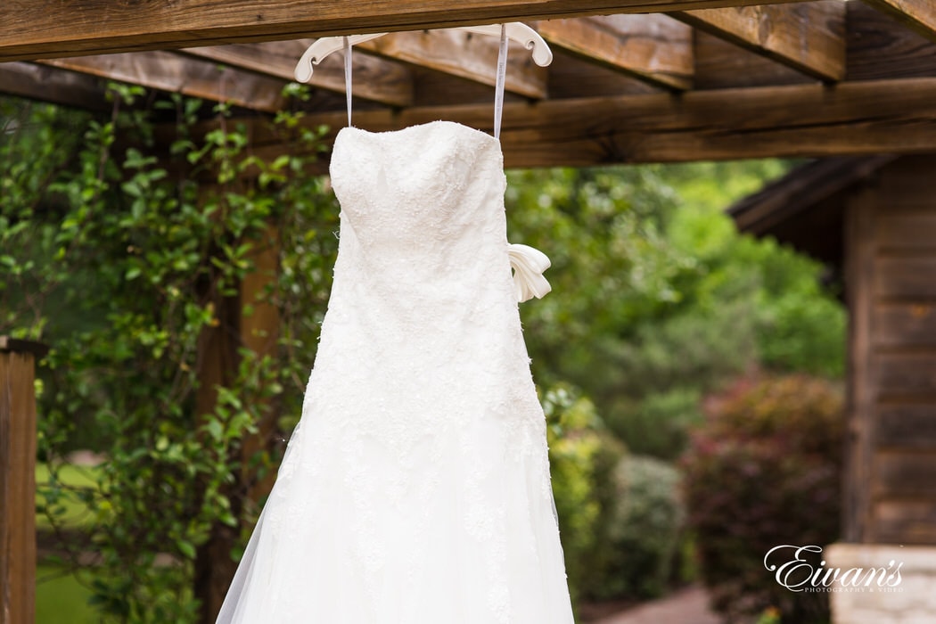 Stunning bride's gown hanging against rustic wood and vibrant greens.