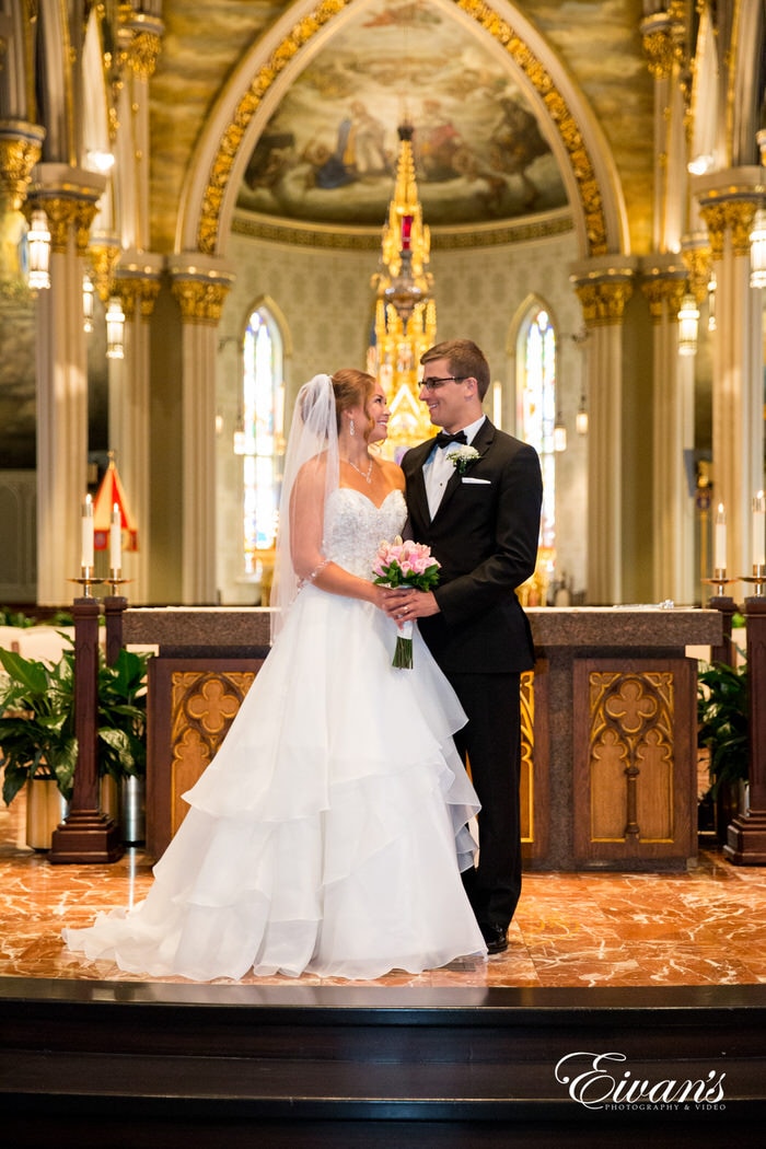 The couple stands at the front of the alter of this stunning chapel just gazing into one another's eyes. The look being shared between the two love birds is undeniable and demonstrates only true love and pure chemistry.