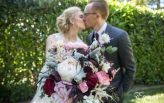 Holding her vintage and stunning maroon and pink floral bouquet with them kissing and celebrating themselves and their marriage.