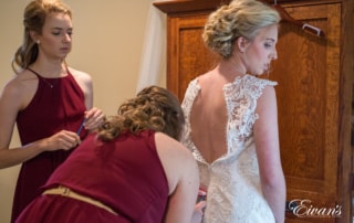 The bridesmaids help zip the bride into her stunning wedding dress that is just so perfectly fitting on her.