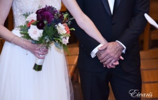 The groom holds his bride's while standing at the alter together.