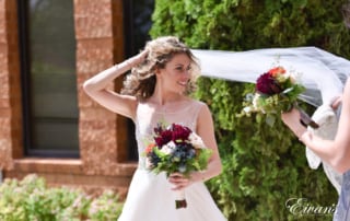 The bride smiles beautifully as her bridesmaids help elegantly arrange her veil.