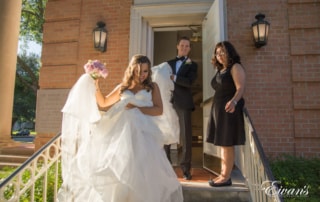 The groom helps carry his bride's gown down the steps as they exit the chapel.