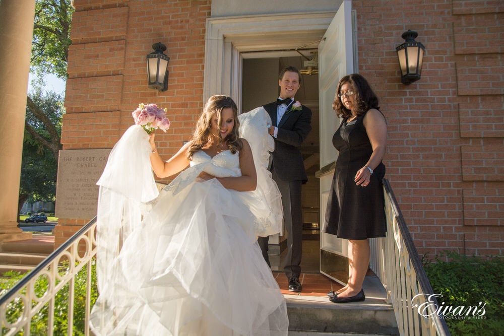 The groom helps carry his bride's gown down the steps as they exit the chapel.