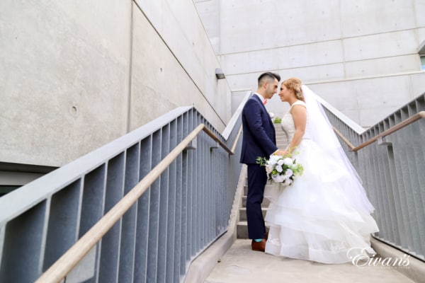 The bride and groom hold one another while standing on a stunning and beautiful stairwell.