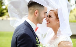 The bride and groom gaze deeply and passionately into one another's eyes with the beauty of the bride's veil.