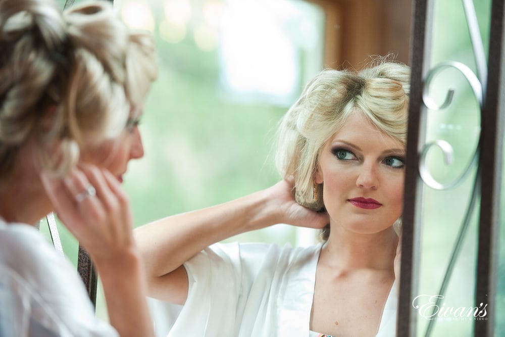 The bride looks at her stunning makeup while waiting for her hair to curl perfectly.