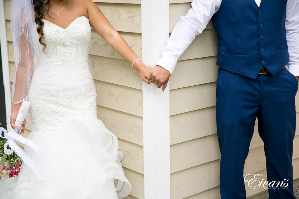 The bride and groom hold hands around a corner unable to see one another before the walk down the alter.