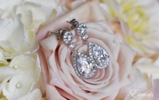 The bride's stunning jewelry effortlessly lays upon a light pink rose that is in her beautiful bouquet.