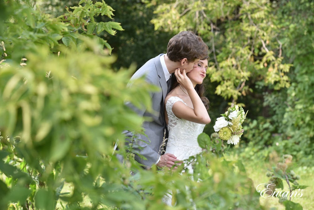 The groom kisses the cheek of his bride while they are entirely surrounded by mother nature.