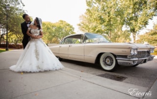 The groom embraces his bride in front of an old 1950's cadillac giving this couple a different edge to their wedding.