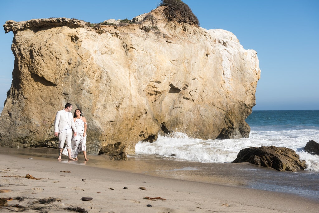 engaged man and woman walking on the beach during the daytime