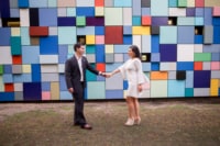 eivans_gallery_engagement_photos_108 A newly engaged couple stand face to face holding hands in front of a multi-colored, geometric wall.