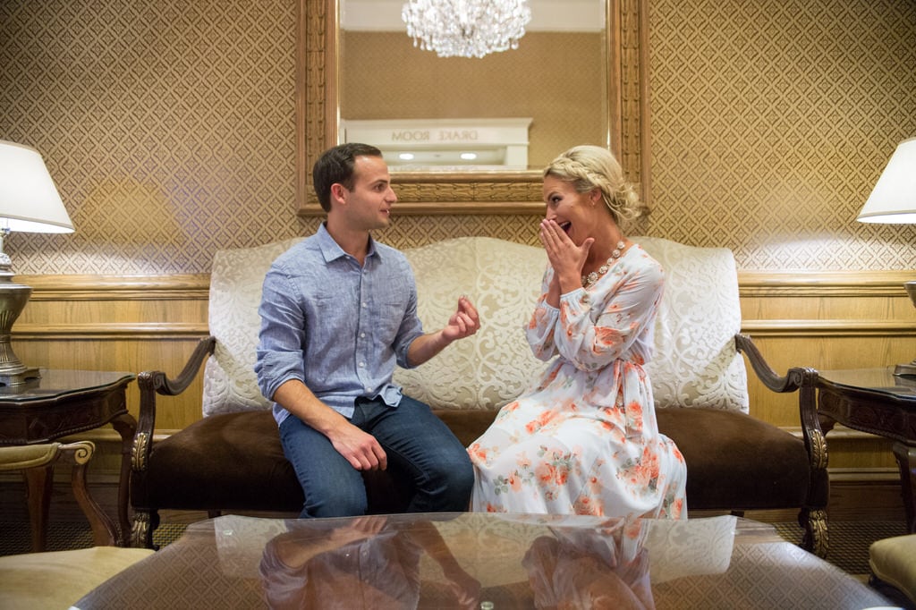 A man proposes to his girlfriend in a beautiful, old-fashioned room. The woman looks at him with excitement in her eyes and covers her mouth with her hands.