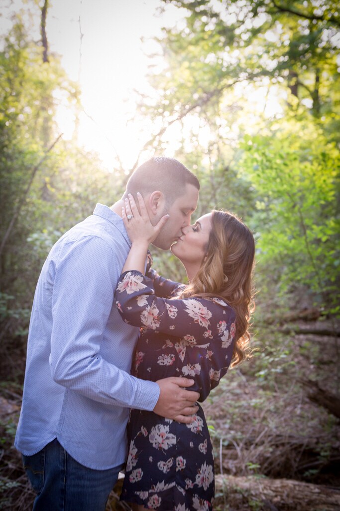 A newly engaged couple kiss each other passionately in the middle of the forest.