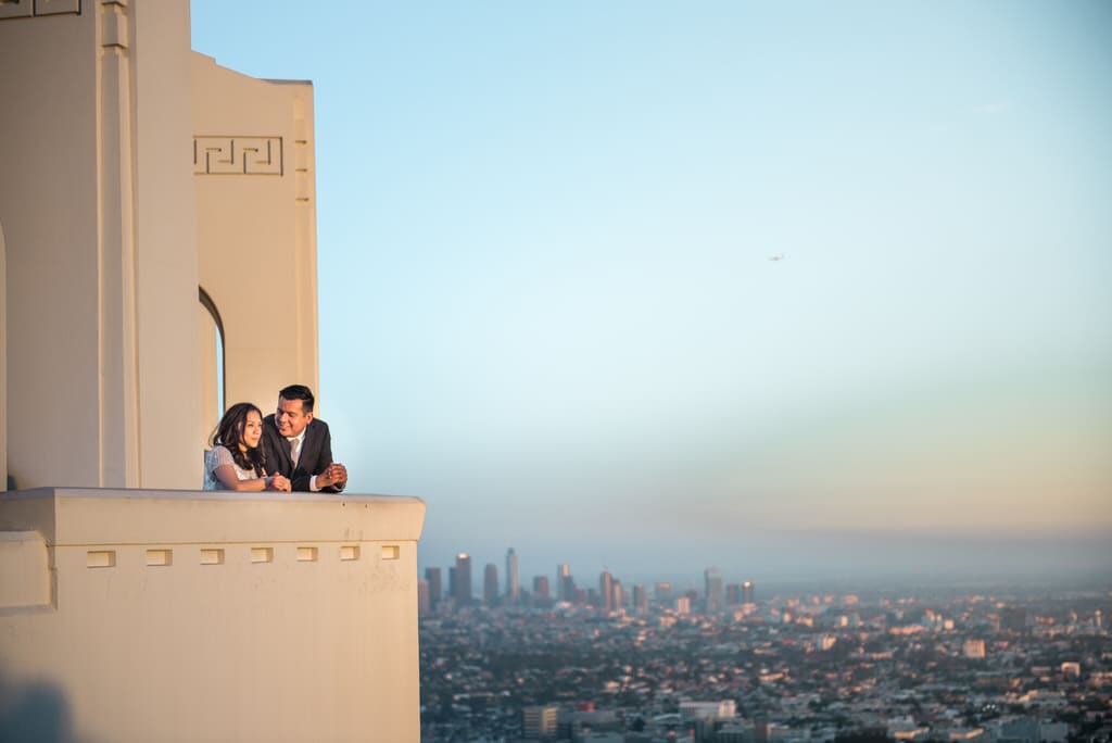A newly engaged couple admires the city below them as the sun begins to set.