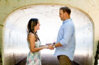 Brooke & Patrick Ganzak A newly engaged couple hold hands and smile at one another in front of a wide tunnel.