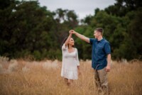 Cristi & Justin 5/5/18 A man twirls his soon-to-be bride in the middle of a tall field surrounding by trees.