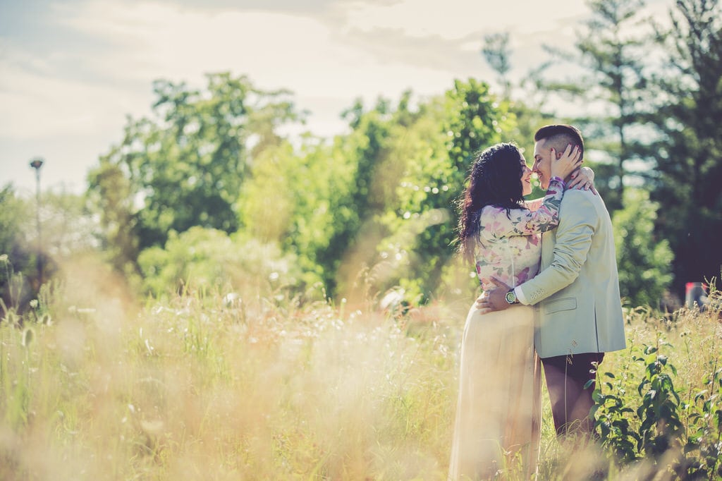 A young couple holds each other close on a sunny day in a tall field.