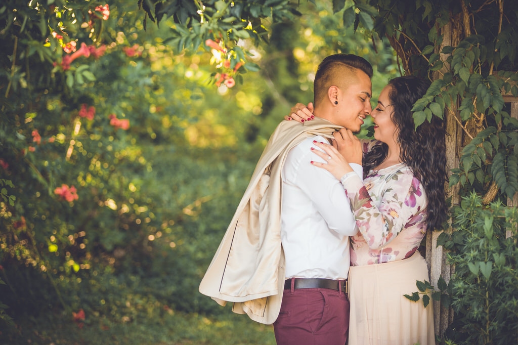 A hot latino couple goes in for a kiss underneath a coral hibiscus archway in the summer.