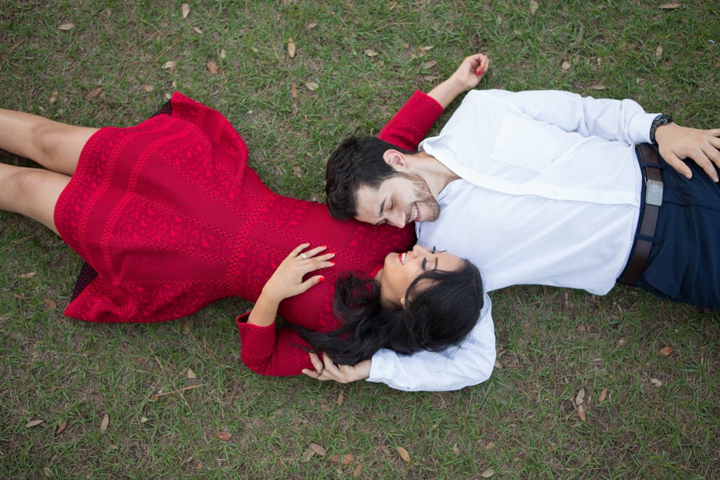 This couple lays on the their backs in this beautiful field. The soon-to-be bride is dressed in a bright red dress that is compared with the soon-to-be groom's classic white blouse and navy blue pants. The vivid red on the dress really makes the couple and their pearly white smiles pop.