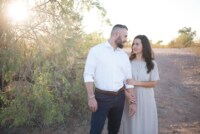 eivans_gallery_engagement_photos_153 This couple looks lovingly at one another while walking down the sandy beach. The bright green plants with the shining sun help demonstrate and represent the love shining through this couple's bones