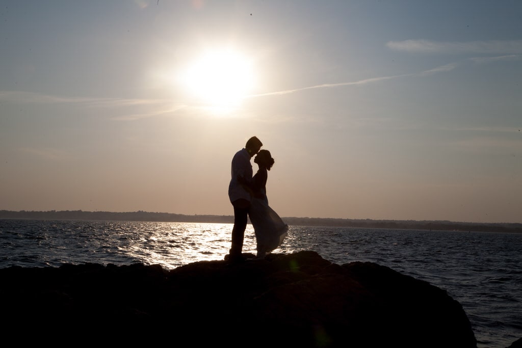 This loving couple holds one another on a set of rocks looking out at the sparkling water. The sun shining on the sparkling water while they spend an intimate moment together in one of the most romantic places in the world.