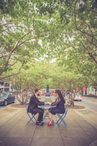 Wedding / Engagement Photography This couple sits at a bright blue set of tables and chairs while it is placed in the center of a very busy road. They hold hands and smile relentlessly because all they are sharing is their everlasting love. The red and blue in the scenery is complemented by the couple's looks, it makes this photograph more than pleasing to the eyes.