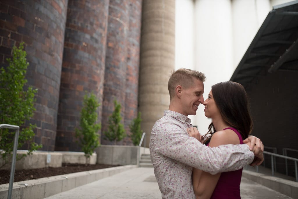 A young man holds his new fiance tightly as their nose's touch and they smile at each other.