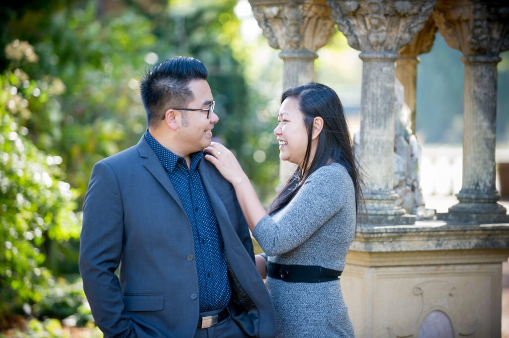 A newly engaged couple smile and laugh with one another on a sunny day.